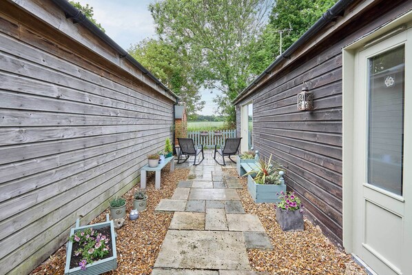 A narrow outdoor patio with stone flooring, wooden walls, and potted plants.