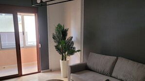 A modern living room with a grey sofa, a small round table, a potted plant, and a ceiling light fixture. - Chic 1-bedroom apartment with WiFi, AC in beautiful Durrës near the sea (Durrës)