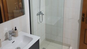 A modern bathroom with a glass-enclosed shower, a white sink with a mirror, and a wooden door. - Chic 1-bedroom apartment with WiFi, AC in beautiful Durrës near the sea (Durrës)