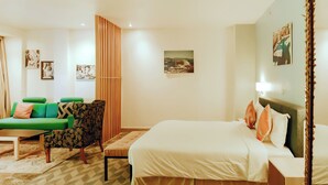 Une chambre d’hôtel avec un lit, un canapé vert, un fauteuil à motifs et une petite table.