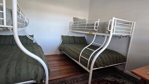 Una habitación con dos literas, cada una con ropa de cama y almohadas verdes, piso de madera y una pequeña mesa de madera.