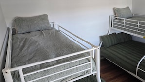 Una habitación con dos literas, una con una manta gris y la otra con una manta verde a rayas.