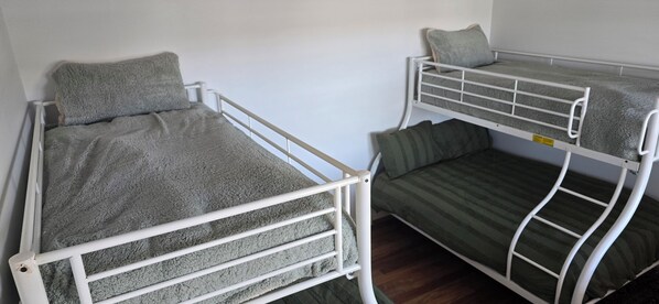 Una habitación con dos literas, una con una manta gris y la otra con una manta verde a rayas.