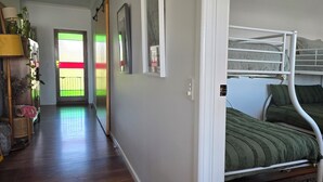 Una habitación con literas, piso de madera, una puerta con un panel de vidrio de colores y un pasillo con estante para plantas.