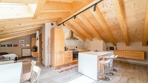 Une cuisine moderne avec des poutres en bois, un îlot central, des tabourets de bar et un coin repas avec des chaises.