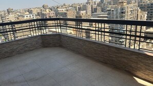A balcony with a stone wall and metal railing, overlooking a densely packed urban area with numerous buildings.