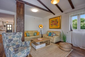 A living room with a sofa, a coffee table, and a chair with a leaf pattern. There is a painting on the wall and a window with curtains. - Villa Kristina With Pool (Tar-Vabriga)