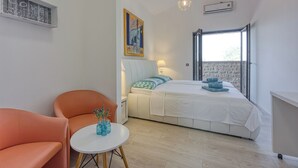 Une chambre à coucher moderne avec un lit, une petite table sur laquelle est posé un vase, deux fauteuils orange, un tableau au mur et une fenêtre donnant sur un paysage.