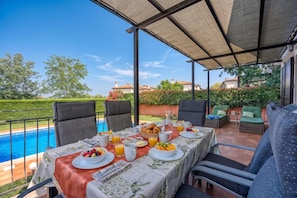 Ein Essbereich im Freien mit Blick auf einen Pool, überdachter Sitzbereich und ein für das Frühstück gedeckter Tisch.