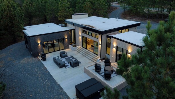Une maison moderne dotée d’un patio couvert, de grandes fenêtres et d’une vue sur la forêt.