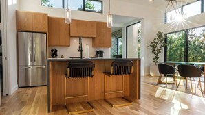 Une cuisine moderne avec des meubles en bois, un réfrigérateur en acier inoxydable et un coin bar équipé de tabourets.