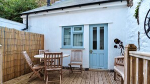 A wooden deck with a table and chairs, a blue door, and a white wall. - Nor Nour, Cawsand (Cawsand)