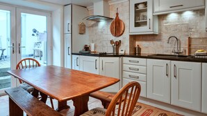 A modern kitchen with white cabinets, a wooden dining table, and a large window. - Nor Nour, Cawsand (Cawsand)