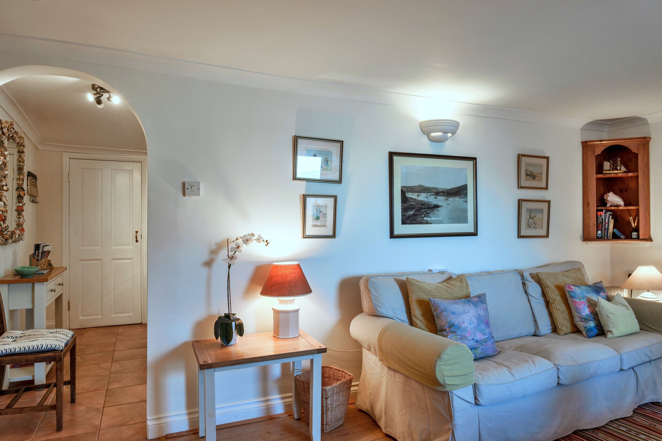 A living room with a sofa, a table with a lamp, and framed pictures on the wall.