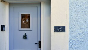 A white door with a keyhole and a small window. There is a black sign on the wall next to the door that reads "Nor Nour." - Nor Nour, Cawsand (Cawsand)