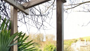 Un banco de madera con cojines, una pérgola de madera y vistas al jardín.
