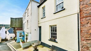 A narrow street with traditional buildings, including a white house with a blue door and a brick house.