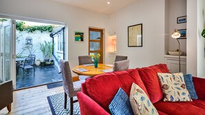 A modern living room with a red sofa, a wooden dining table, and a small kitchen area.