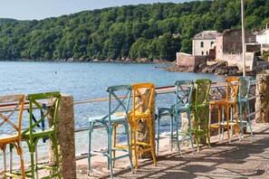 A row of colorful chairs along a waterfront with a stone wall and a building in the background. - Rose Cottage, Kingsand (Kingsand)