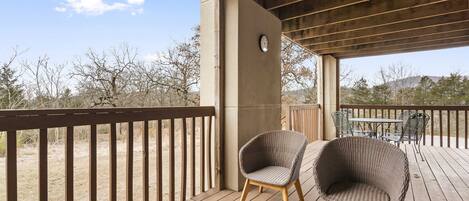 Eine Holzterrasse mit zwei Korbstühlen, einem Tisch und einer Uhr an der Wand.