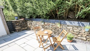 A patio with a stone wall, a wooden table, and chairs. - Little Birchinlea (Glossop)