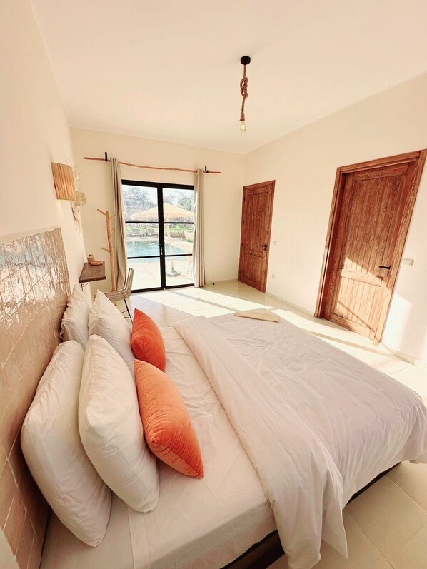 A bedroom with a large bed, a view of a pool, and a wooden door. - Luxury Getaway: Elegant Villa with a Pool and Privacy (Essaouira)