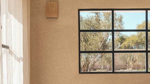 Una habitación con una cama, una ventana con vistas a árboles y una lámpara en la pared.