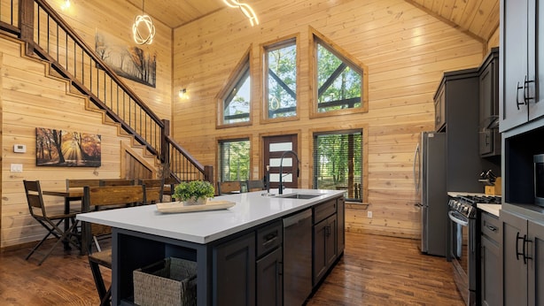A spacious kitchen with a large island, dark cabinetry, and a wooden floor. - Cozy Cabin with Hot Tub, Fire Pit & Arcade Games (Broken Bow)
