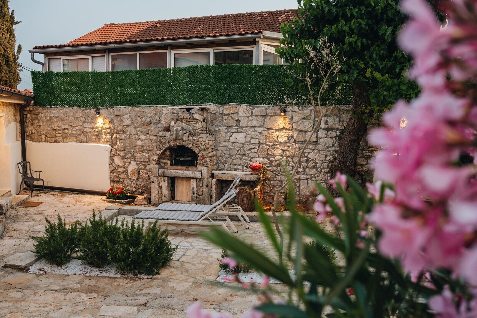 A stone wall with a built-in fireplace, a lounge chair, and a potted plant.