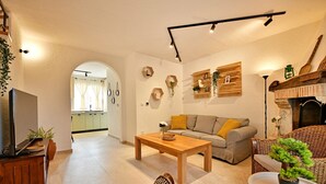 A modern living room with a sofa, coffee table, and wicker chairs. There is a television on a wooden stand and a fireplace with a stone mantle. - Holiday house Vento (Poreč)