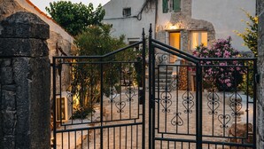 A gated entrance with a stone wall and a building with a stone facade and green shutters. - Holiday house Vento (Poreč)