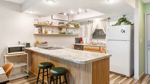 A modern kitchen with a central island, wooden cabinets, a white refrigerator, and a microwave on a cart. - Mossy Pines of the Ozarks (Branson)