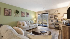 A living room with a sofa, a coffee table, and a dining area with a table and chairs. There are framed pictures on the wall and a window with a view of trees. - Mossy Pines of the Ozarks (Branson)
