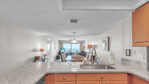 A kitchen with wooden cabinets, a granite countertop, and a view to the living area.