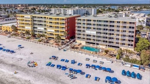 A beachfront hotel with multiple floors, a swimming pool, and a sandy beach with sun loungers.
