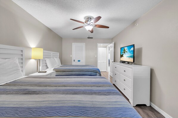 A bedroom with two beds, a ceiling fan, a TV, and a dresser.
