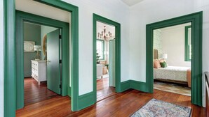A hallway with green door frames leading to a bedroom with a bed, a nightstand, and a lamp.