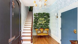A staircase leading to a room with a blue door, a wall-mounted plant wall, and a yellow sofa with patterned cushions.