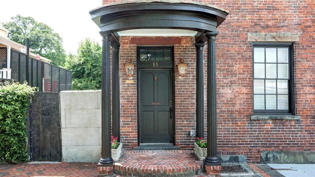 A brick building with a black door, a small porch with steps, and a window to the right.