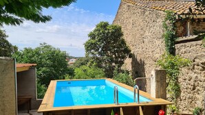 Una terraza de madera con piscina, rodeada de plantas en macetas y un edificio de piedra.