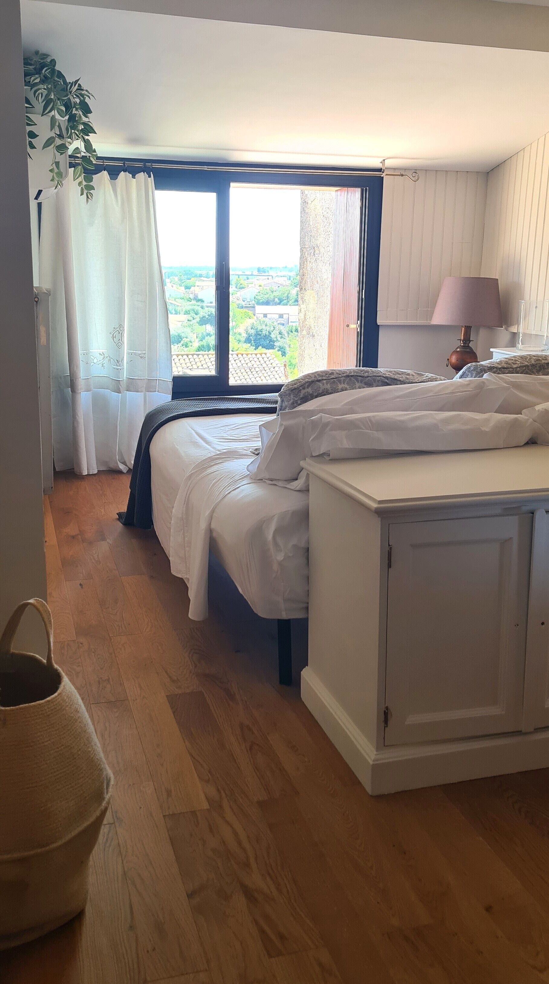 A bedroom with two beds, a window with curtains, a bedside lamp, and a view of the outside.