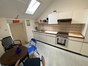 A compact kitchen with a skylight, white cabinets, a stove, and a dining area with a table and chairs.