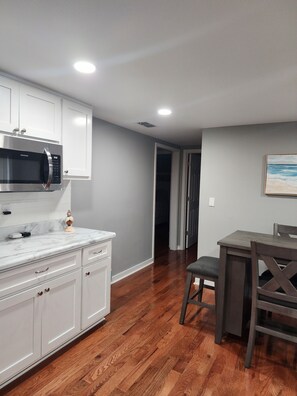 A modern kitchen with white cabinetry, a built-in microwave, and a marble countertop.