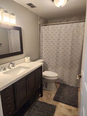 A bathroom with a white sink, dark wooden vanity, a mirror, a toilet, and a shower curtain.