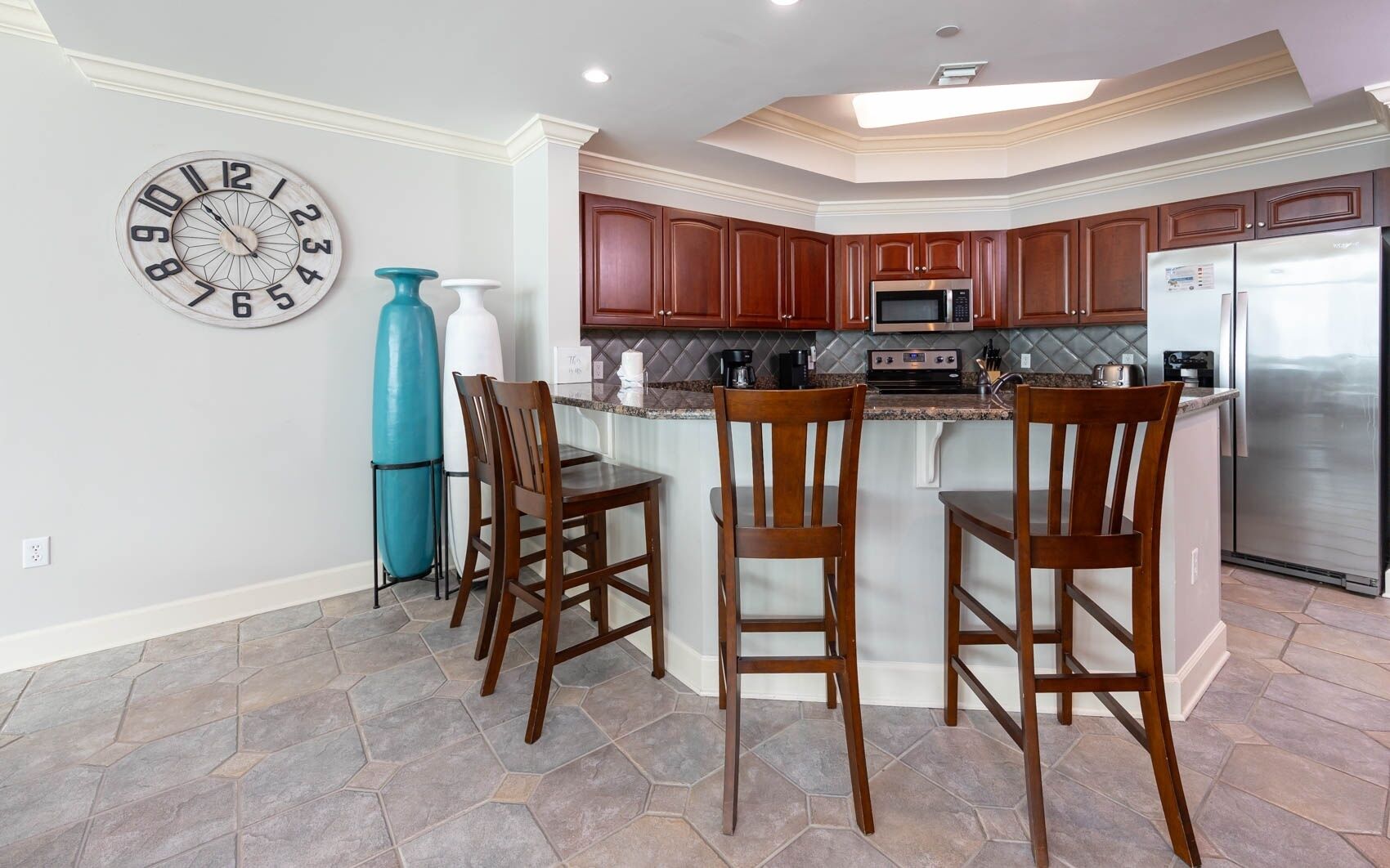 A modern kitchen with wooden cabinets, a stainless steel refrigerator, a microwave, and a large island with bar stools.