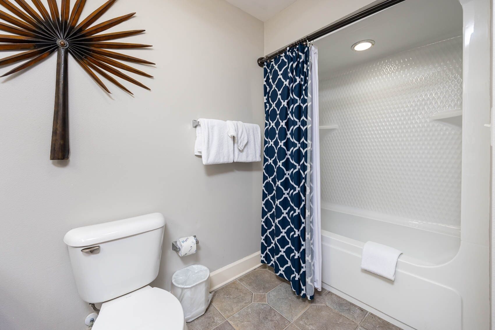 Une salle de bain équipée de toilettes, d’une poubelle, d’un rideau de douche et d’un élément décoratif mural.