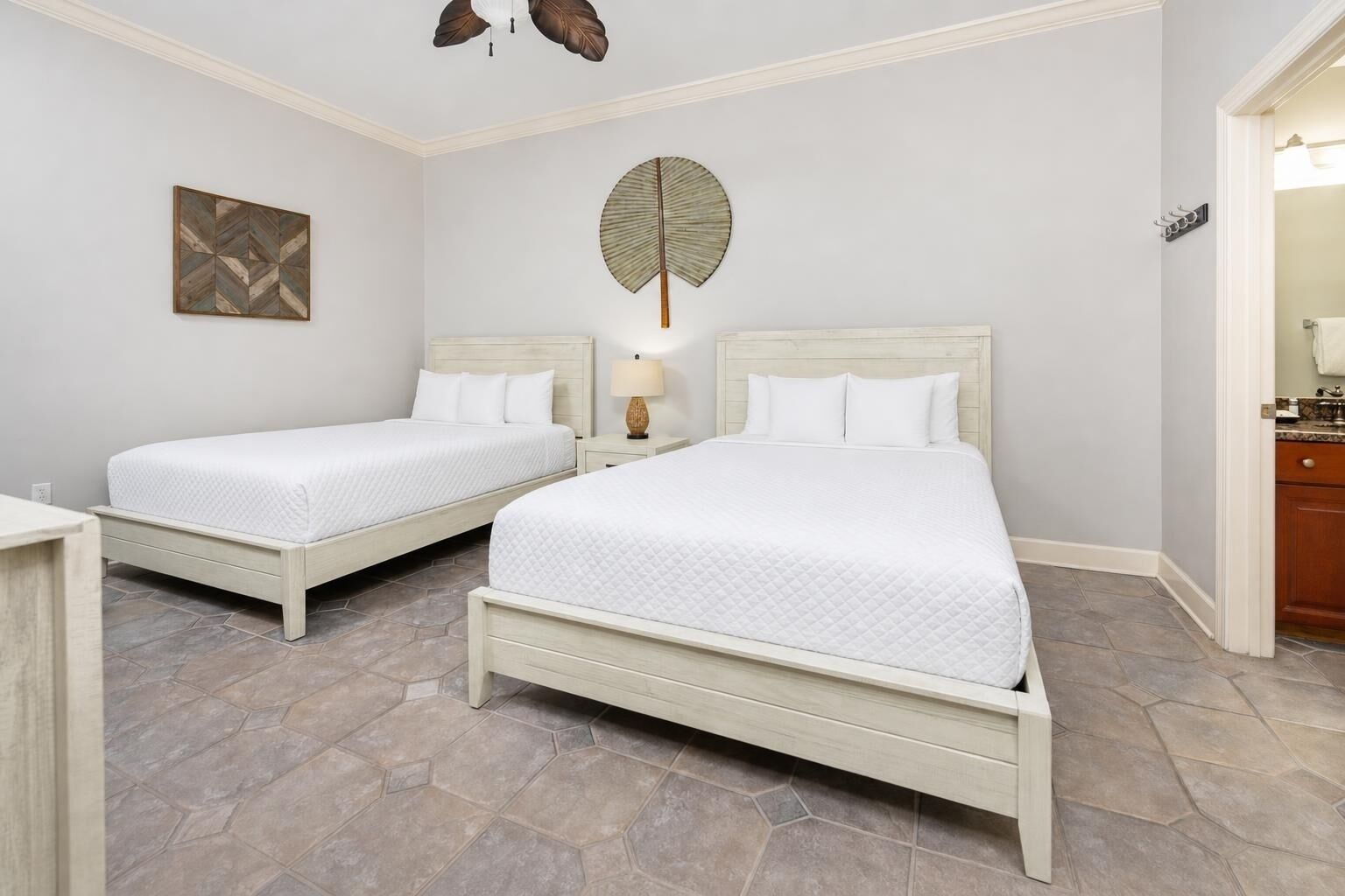 A hotel room with two beds, a ceiling fan, a wall art piece, and a nightstand with a lamp.