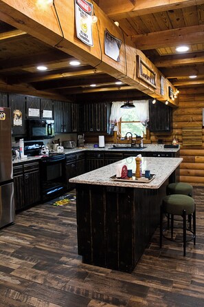 A rustic kitchen with wooden cabinets, a large island, and a refrigerator. - Cozy Cabin, Leaves 🍁 Private Swim Jacuzzi Spa- Beautiful Gardens & Orchard   (Jonesborough)