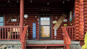 A rustic log cabin with a porch, a wooden sign reading "MARIN'S CAMPSTOVE," and a small garden with yellow flowers.