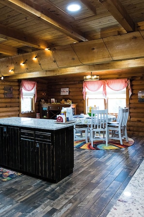 A rustic cabin interior with a kitchen area, dining table, and chairs. - Cozy Cabin, Leaves 🍁 Private Swim Jacuzzi Spa- Beautiful Gardens & Orchard   (Jonesborough)